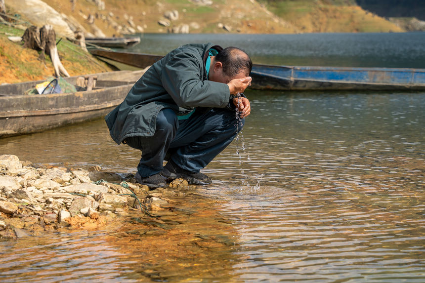 派送完畢后,張林昌在江邊等候渡船返回的間隙用江水洗臉。人民網 涂敏攝