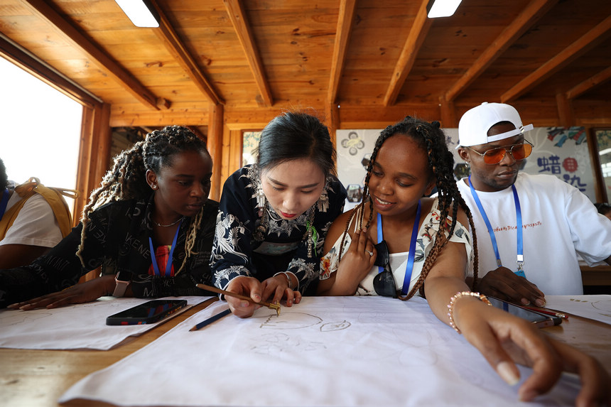 7月21日，非遺傳承人張義蘋（中）在向留學生示范苗族蠟染繪畫技藝。