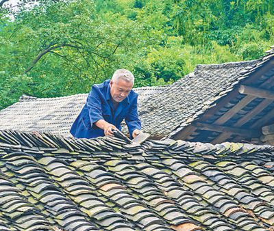 圖為萬明春在撿瓦,修補漏雨的地方。蘇 濱 涂 敏攝影報道