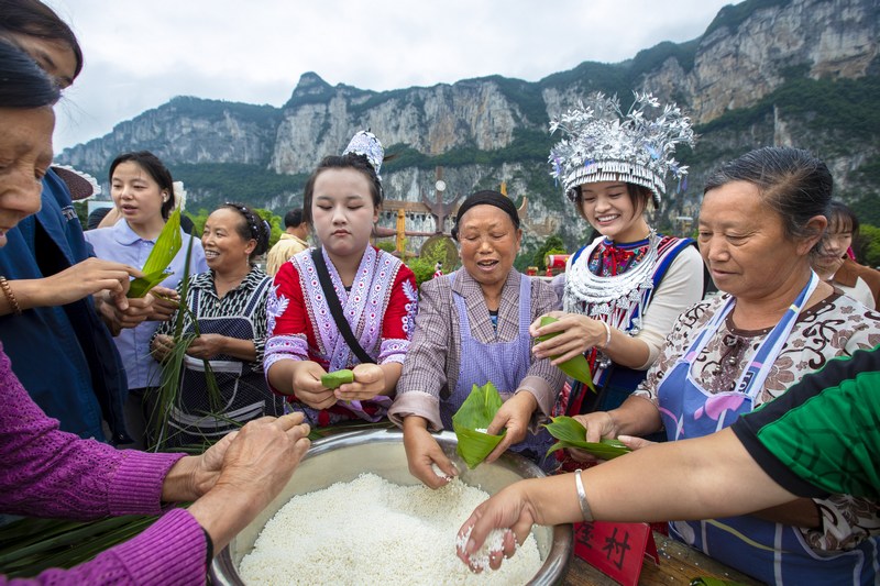 6月7日，貴州省畢節市黔西市新仁苗族鄉化屋村，村民們和游客包粽子。
