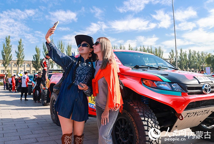 8月22日,外國游客在中國庫布齊沙漠越野賽暨中國汽車越野拉力錦標(biāo)賽杭錦旗分站賽開幕式活動現(xiàn)場打卡留影。丁根厚攝