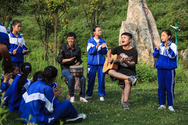 顧亞與鄭龍校長和孩子們在草坪上彈琴互動。