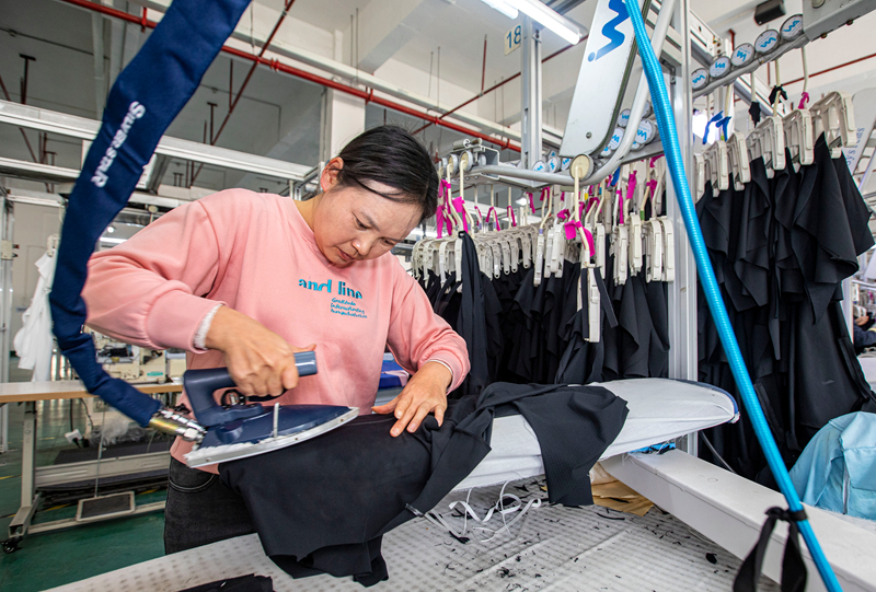 工人在貴州省畢節市黔西市經濟開發區一家服飾企業車間生產線上熨燙服飾。