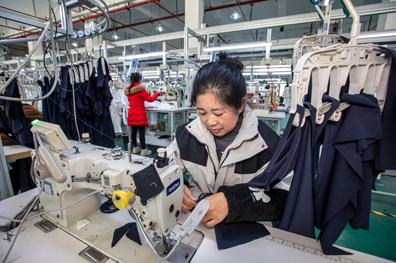工人在貴州省畢節市黔西市經濟開發區一家服飾企業車間生產線上加工服飾。