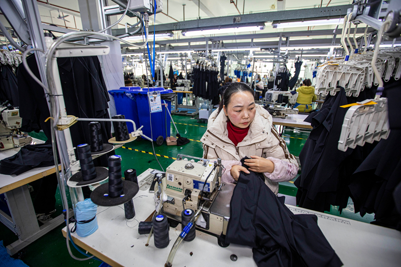 工人在貴州省畢節市黔西市經濟開發區一家服飾企業車間生產線上加工服飾。