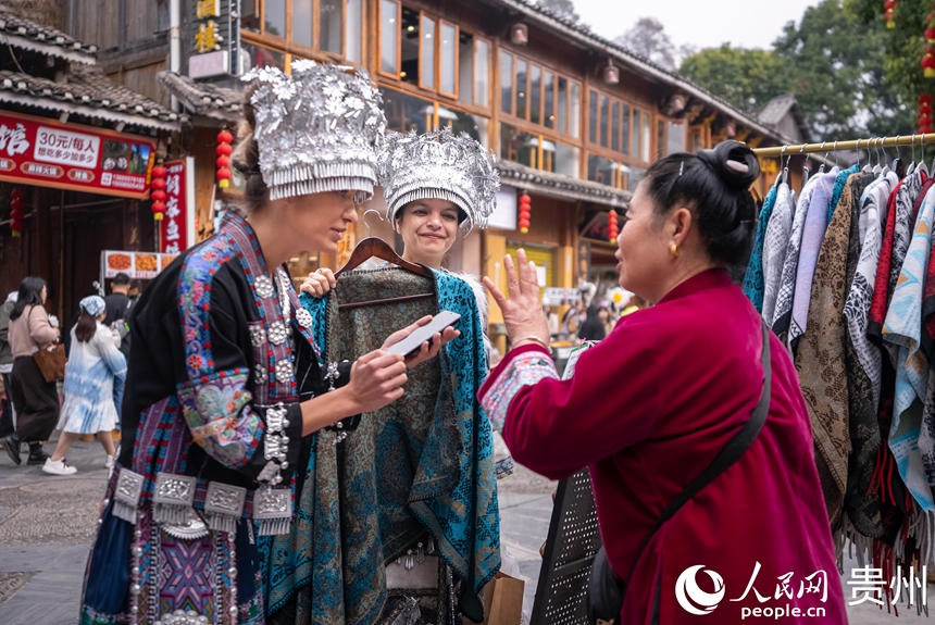 12月20日，來自國外的游客身著當地少數民族同胞盛裝選購商品。人民網記者 涂敏攝