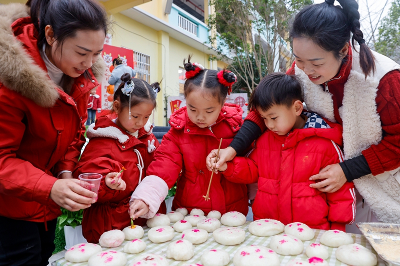 2025年12月31日，貴州省黔東南苗族侗族自治州施秉縣第五幼兒園的孩子們在老師的指導下給糍粑蓋紅印。（磨桂賓 攝）