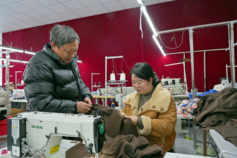 2026年1月12日,貴州省畢節(jié)市納雍縣化作鄉(xiāng)銀鑫制衣廠,負(fù)責(zé)人鄧林海(左)在和員工討論服裝縫制針?lè)ā?